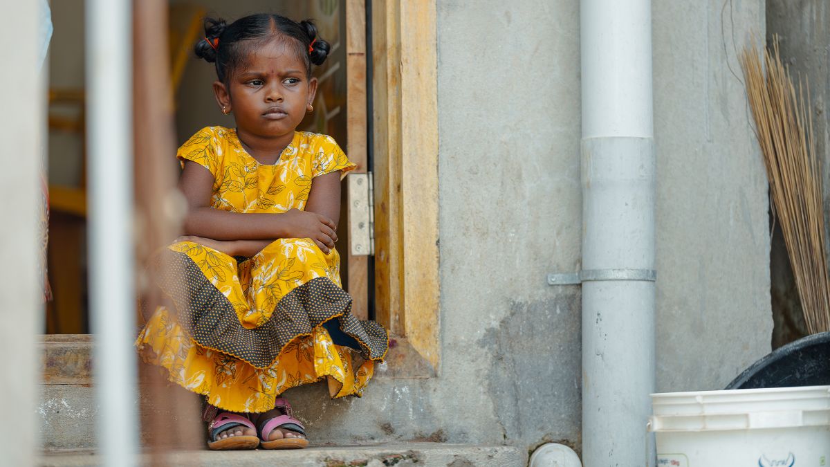 Ein etwa fünfjähriges Mädchen sitzt auf den Stufen eines Hauseingangs.