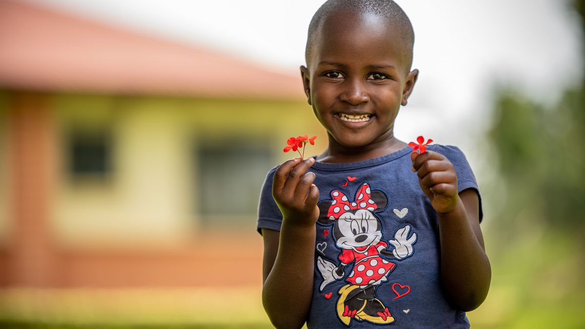 Ein kleines Mädchen hält in beiden Händen rote Blümchen.