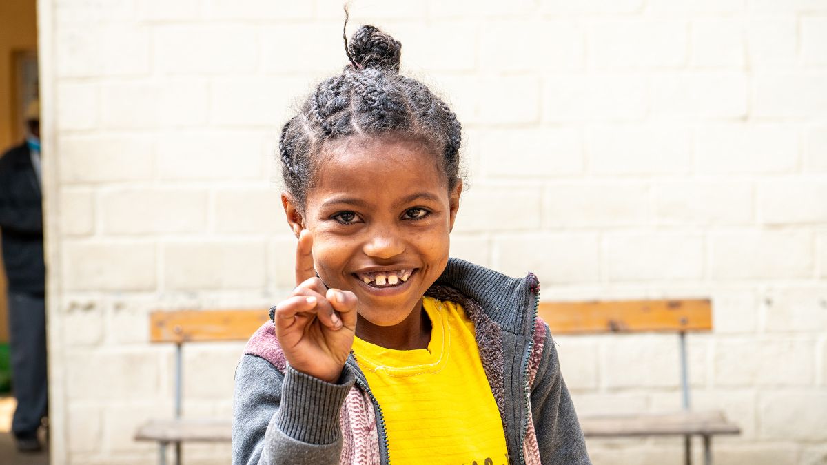 Ein etwa neunjähriges Mädchen steckt lachend den Zeigefinger hoch.