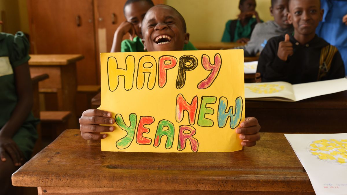 Ein lachender Junge hält in einem Klassenzimmer ein Schild mit der Aufschrift Happy-New-Year