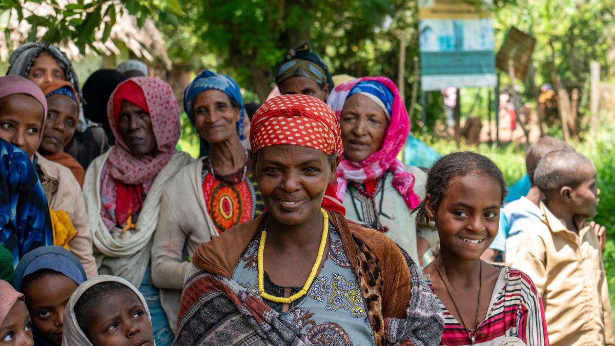 Eine lächelnde Frau ist umringt von Kindern und Erwachsenen.