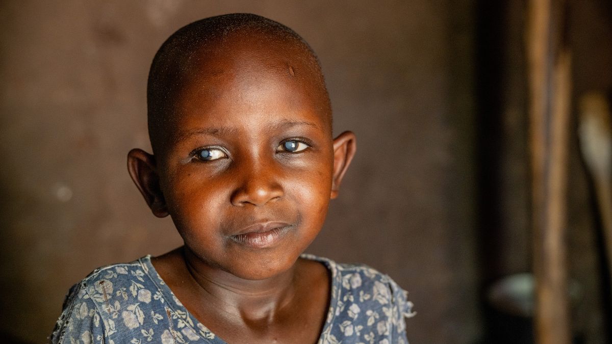 Ein sechsjähriges Mädchen mit hellen Punkten in den Augen. Sie trägt ein blaues T-Shirt mit weißem Blumenmuster.