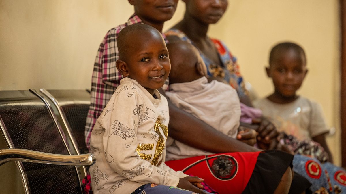 Ein zehnjähriges Mädchen sitzt mit zwei Frau und zwei weiteren Kindern auf einer Wartebank in einem Krankenhaus. 