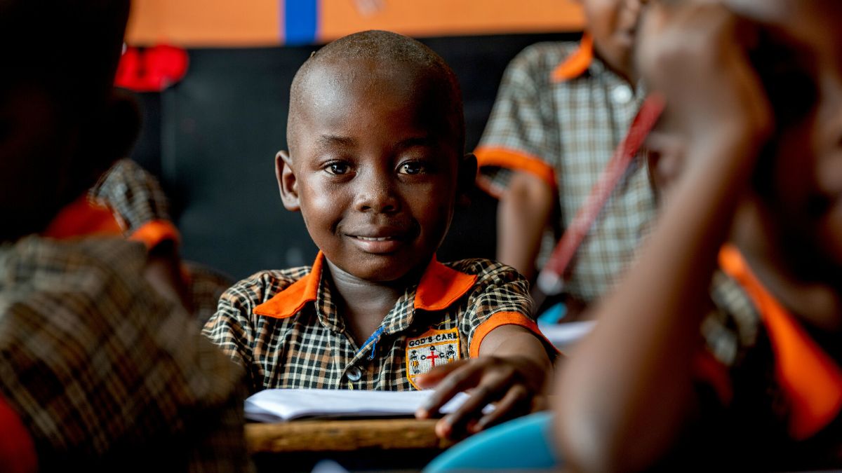 Fünfjähriger Junge sitzt in Schuluniform in seiner Klasse. Er lächelt.