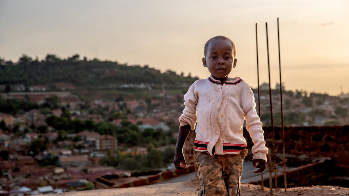 Ein Bild eines Jungen. Im Hintergrund ist die Stadt Kampala abgebildet.