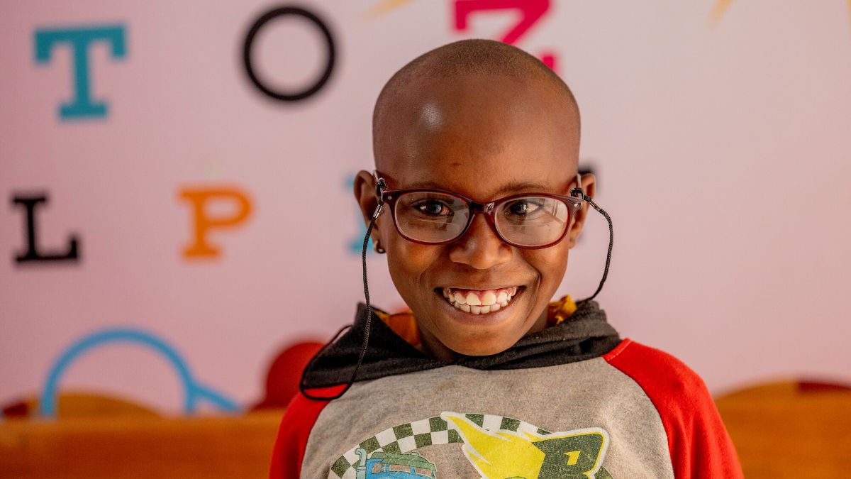 Ein siebenjähriges Mädchen trägt eine Brille mit einer Brillenkette. Sie lächelt.