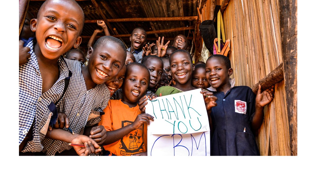 Eine Gruppe lachender Kinder halten zwei Zettel, auf denen steht: Thank you CBM.