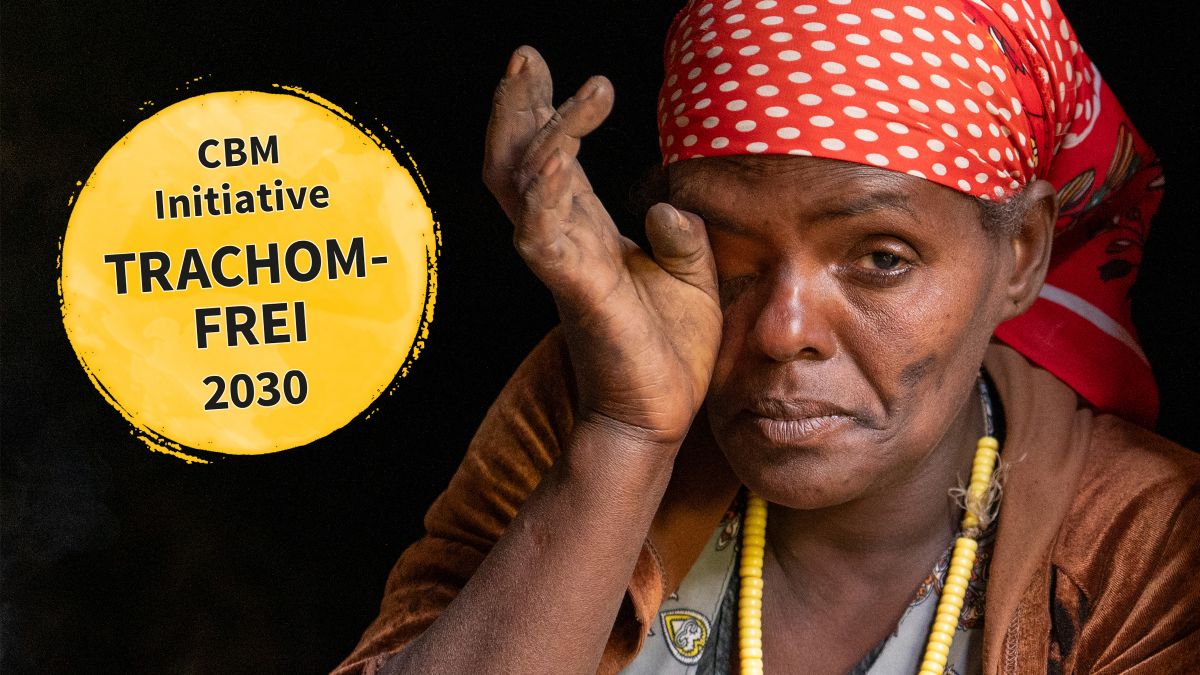 Eine Frau in den Vierzigern mit einem bunten Kopftuch drückt den Rücken ihres Daumens ans rechte Auge. Sie sitzt in der Öffnung einer Lehmhütte. Schriftzug: CBM-Initiative TRACHOMFREI 2030
