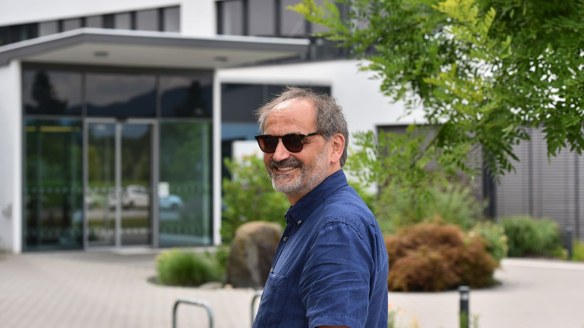 Ein Mann mit Sonnenbrille steht vor einem mehrgeschossigen Bürogebäude.