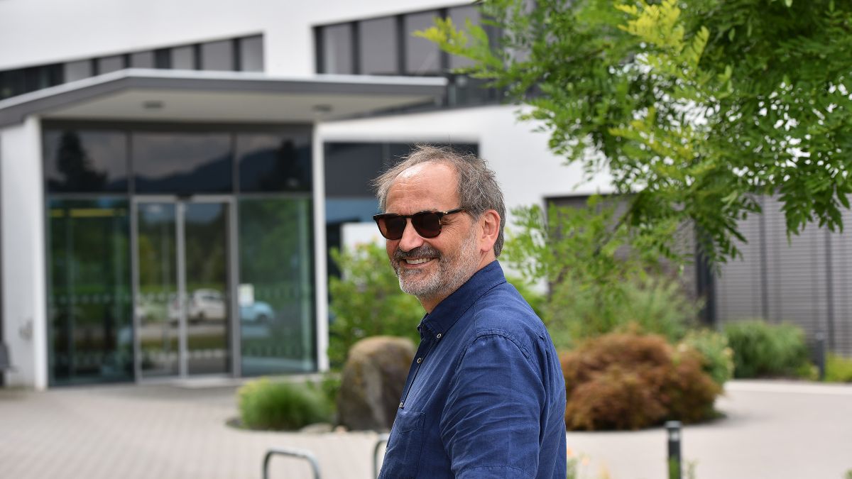 Ein Mann mit Sonnenbrille steht vor einem mehrgeschossigen Bürogebäude.