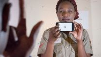 Eine Frau hält ein Smartphone hoch, auf dem ein E zu sehen ist