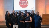 Eine Gruppe aus drei Frauen und sechs Männern in schwarzer Kleidung, an der Wand hinter ihr steht "Chorale Africaine".