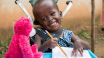 Die sechsjährige Justine aus Uganda wurde mit Hydrozephalus ("Wasserkopf") geboren. Ein CBM-Gemeindehelfer fand die Sechsjährige: Jetzt bekommt sie regelmäßig Physiotherapie und macht tolle Fortschritte. Auf dem Bild freut sie sich über ein Geschenk - einen rosa Teddybären.