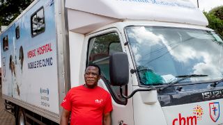 Ein CBM Mitarbeiter steht vor einem Transporter auf dem steht Menog-Hospital