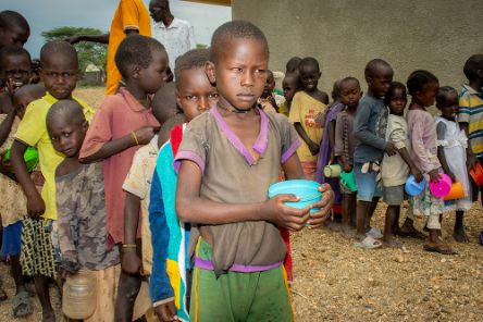 Zwei Reihen von Kindern stehen in der Schlange, in der Hand halten sie Plastikschüsselchen.