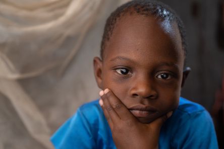 Ein etwa fünfjähriges Mädchen mit weißen Pupillen hat das Kinn auf die Hand gestützt.