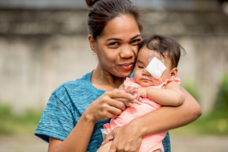 Eine Frau hält ein Baby mit Augenverband im Arm.