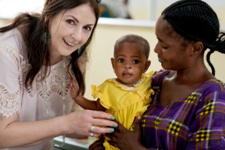 Eine Frau hält ein Baby auf dem Arm. Eine zweite Frau beugt sich zu beiden rüber.