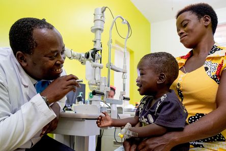 Ein afrikanischer Mann im weißen Kittel leuchtet einem Kleinkind mit einer Taschenlampe ins Auge.