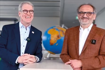 Zwei lachende Herren im Anzug vor einem Globus.