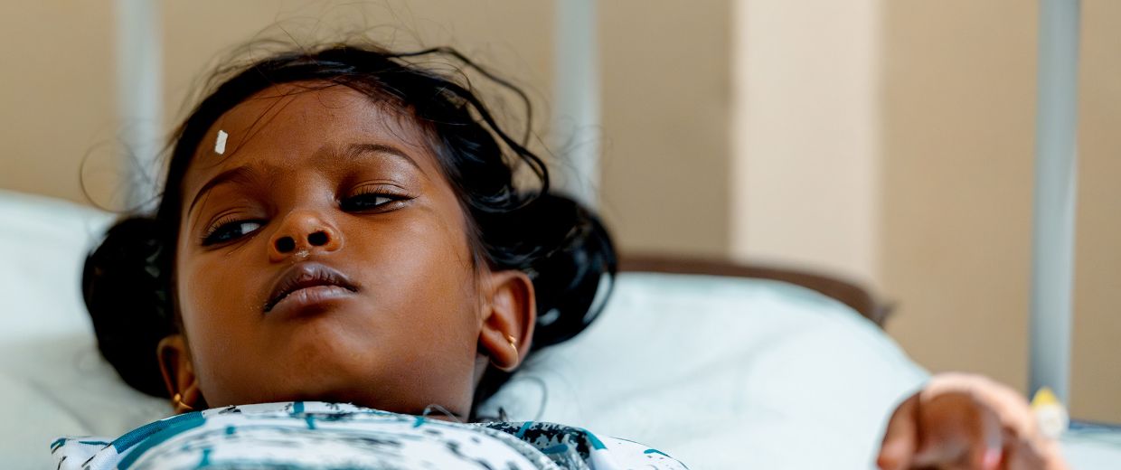 Ein etwa fünfjähriges Mädchen liegt in einem Krankenhausbett. Über dem rechten Auge hat es ein kleines, weißes Markierungspflaster.