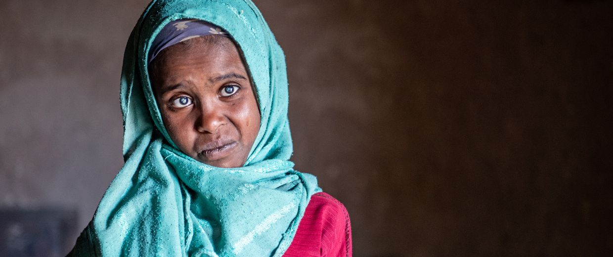 Ein etwa neunjähriges Mädchen mit auffallende weißen Pupillen und einem blauen Kopftuch.
