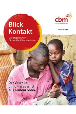Ein kleiner Junge schmiegt sich an die Seite eines Mannes, der auf einem einfachen Holzsessel sitzt.