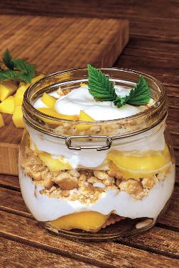 Glas mit Deckel, gefüllt mit weißer Creme, Mangostückchen und Keksbröseln in Schichten