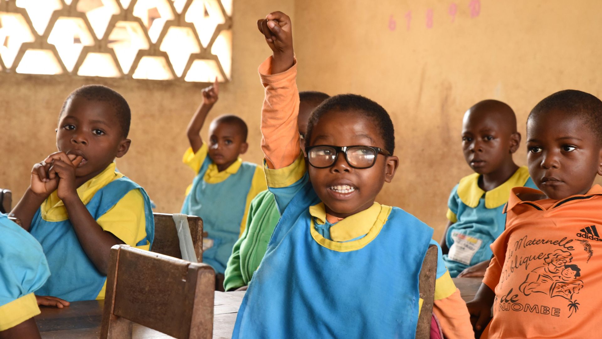 Ein kleines afrikanisches Mädchen mit Brille im Klassenzimmer streckt den Arm hoch.