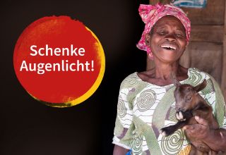 Lachende afrikanische Frau mit einer Ziege auf dem Arm.