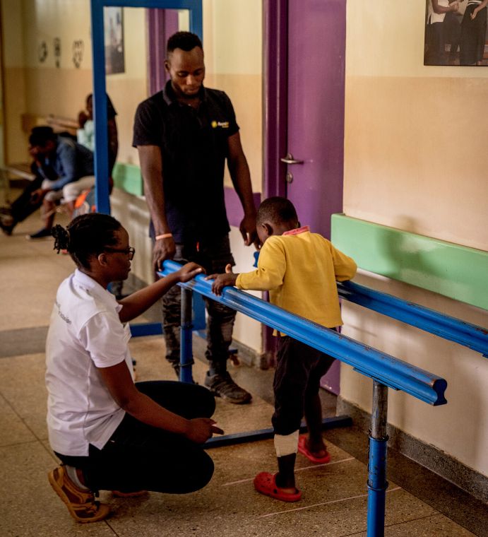 Ein Junge geht an Laufbarren entlang, eine Frau und ein Mann schauen zu.