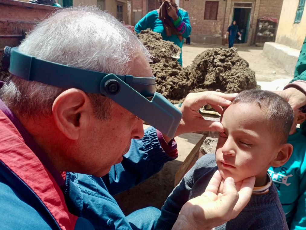 Ein Mann mit Stirnlampe untersucht die Augen eines Kindes.