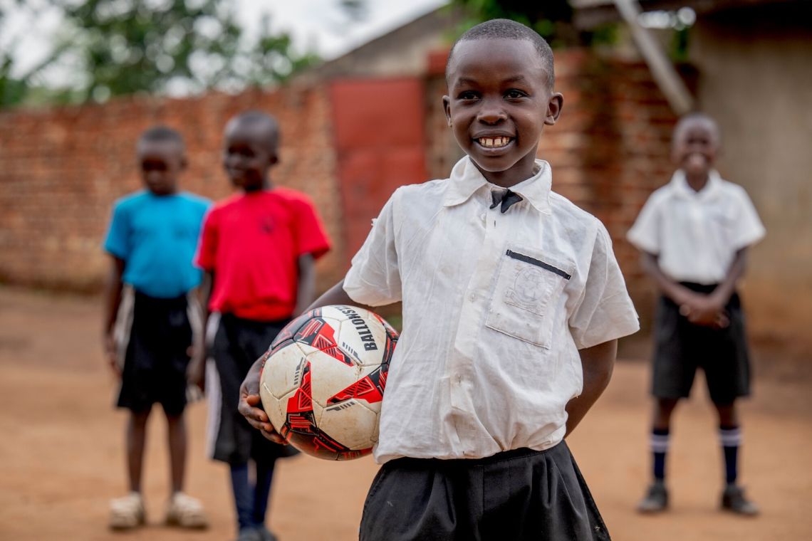 Ein lachender, etwa achtjähriger Junge hält einen Ball im Arm, hinter ihm stehen drei weitere Jungen.