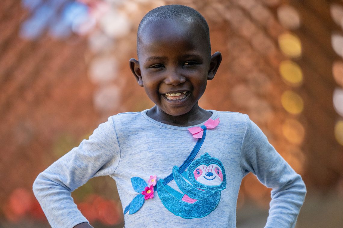 Ein etwa sechsjähriges Mädchen lächelt. Ihre Augen sind etwas gerötet.