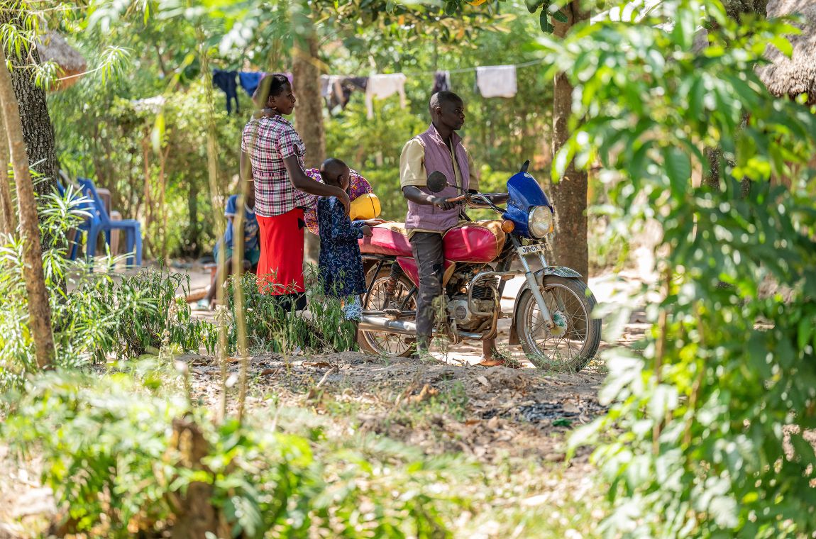 Ein Mann sitzt auf einem Motorrad. Eine Frau, die auf dem Arm ein Kind trägt und ein kleines Mädchen stehen daneben.