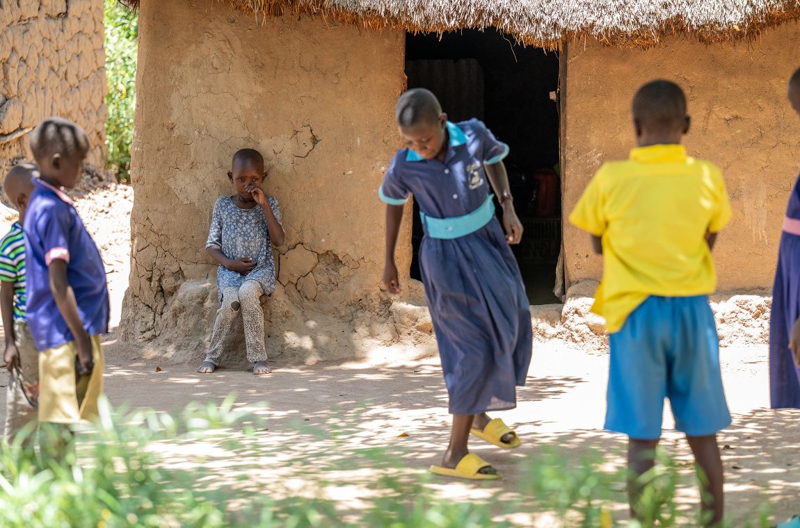 Kinder spielen auf einem Platz. Ein kleines Mädchen sitzt im Abseits und spielt nicht mit.