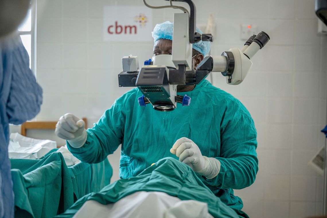 Ein Mann sitzt an einem Mikroskop und operiert die Person, die darunter liegt.