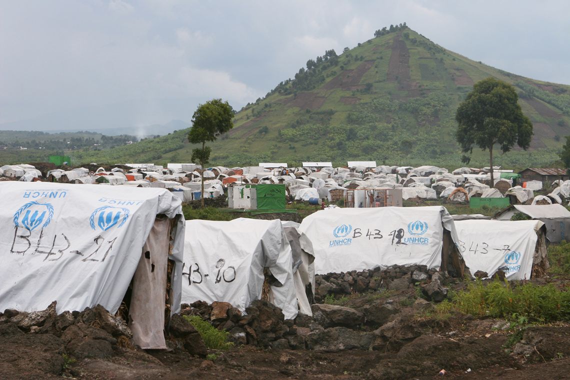 Ein Feld voller Zelte mit der Aufschrift UNHCR vor einem grünen, spitzen Hügel.