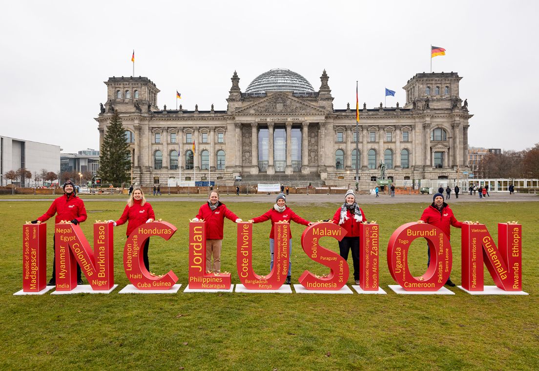 Die Buchstaben mit dem Wort "Inklusion" stehen vor dem Bundestag. Hinter den Buchstaben stehen Mitarbeiter der CBM.