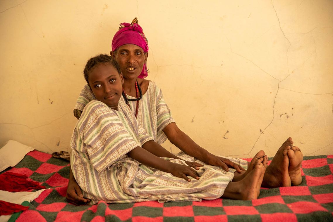 Mulunesh und ihre Mutter sitzen zusammen auf einem Bett.