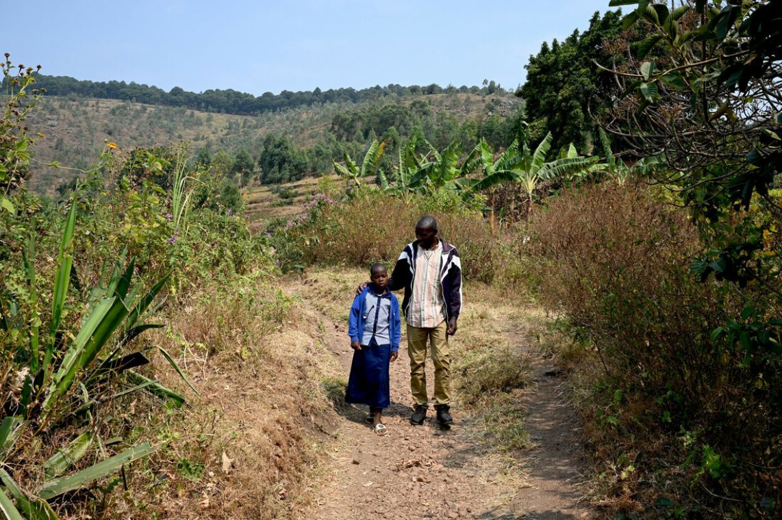 Ein Mann führt ein Mädchen einen abschüssigen Feldweg entlang.