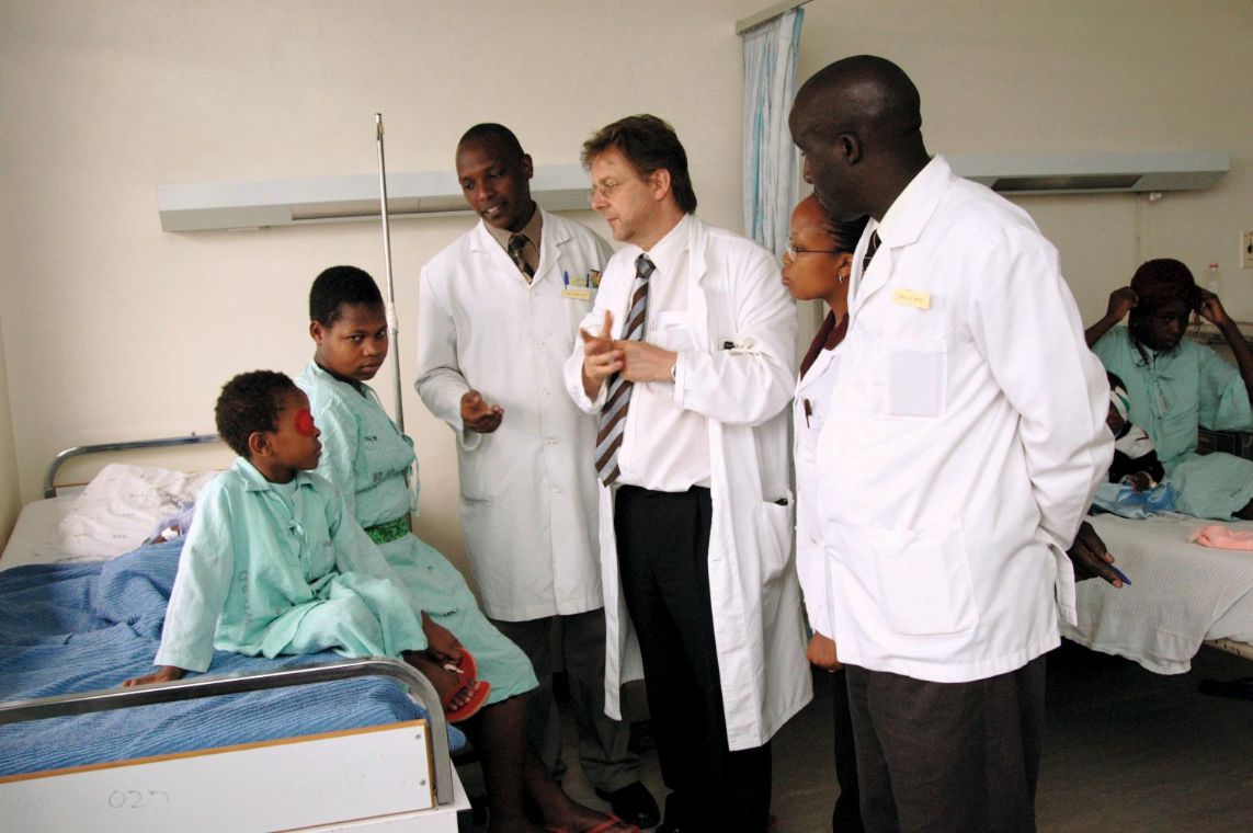 Ärzte und eine Ärztin in weißen Kitteln am Krankenbett eines Kindes.