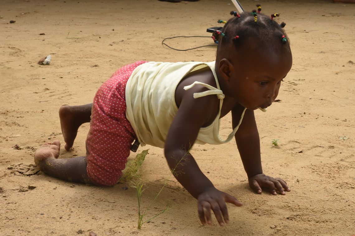 Ein kleines Mädchen krabbelt über sandigen Boden.