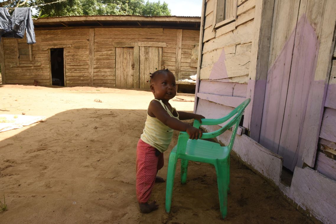Ein Kleinkind steht vor einem Plastikstuhl, an dem es sich festhält.