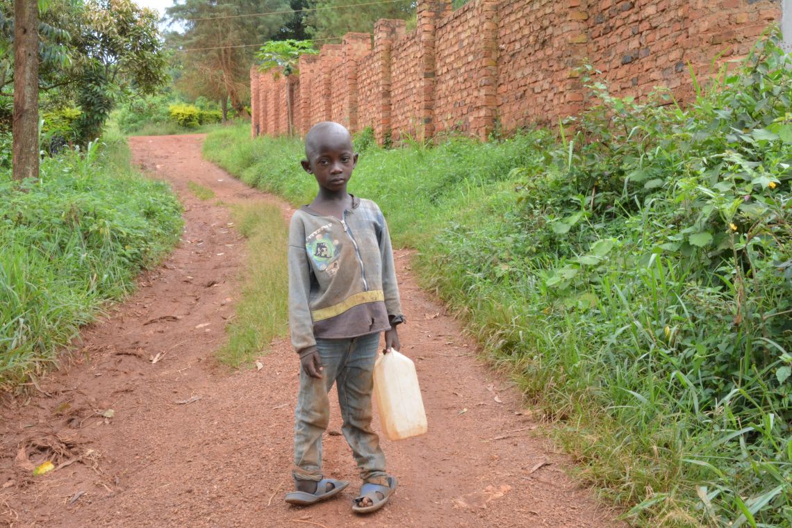 Ein kleiner Junge mit verkümmten Füßen auf einem unbefestigten Weg trägt einen Wasserkanister
