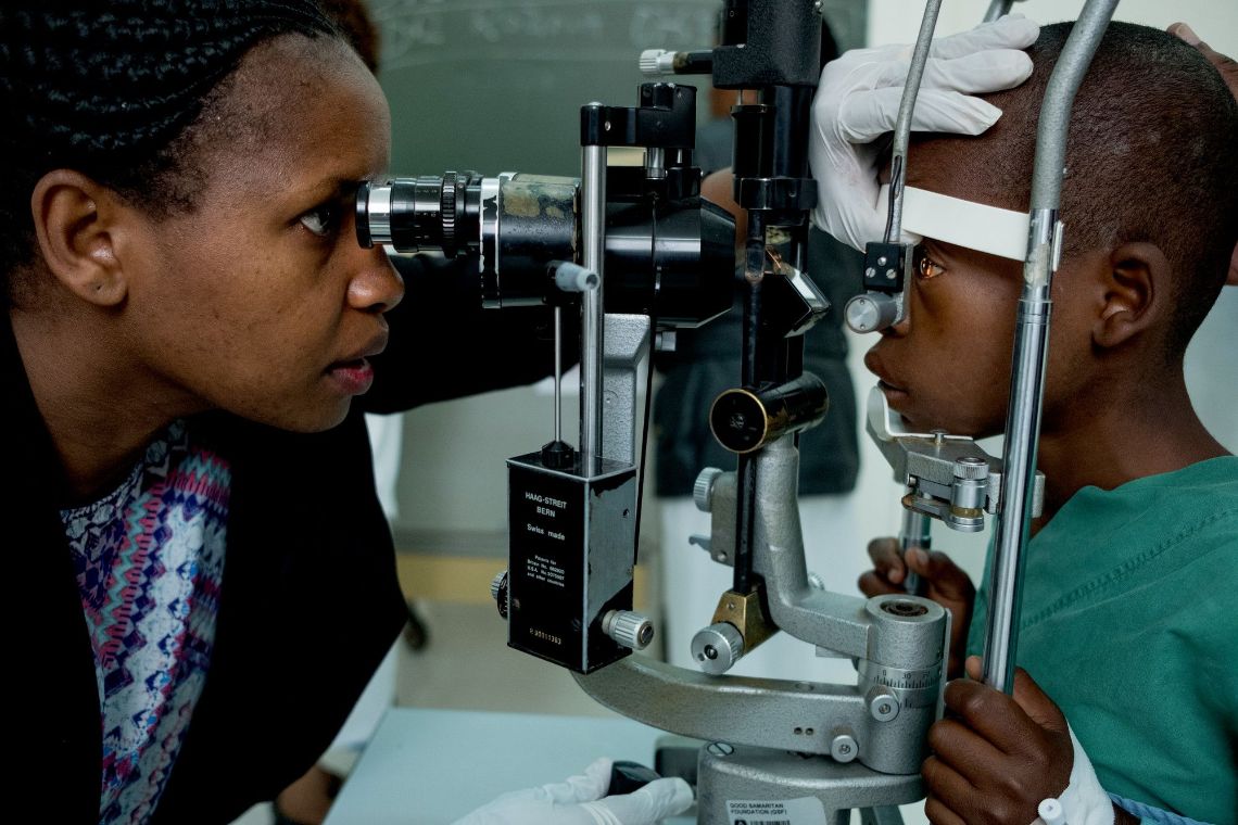 Eine Frau schaut durch ein Untersuchungsgerät in die Augen eines Jungen.