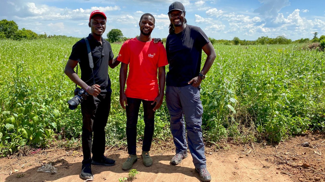 Drei junge lachende afrikanische Männer, im Hintergrund ein Feld