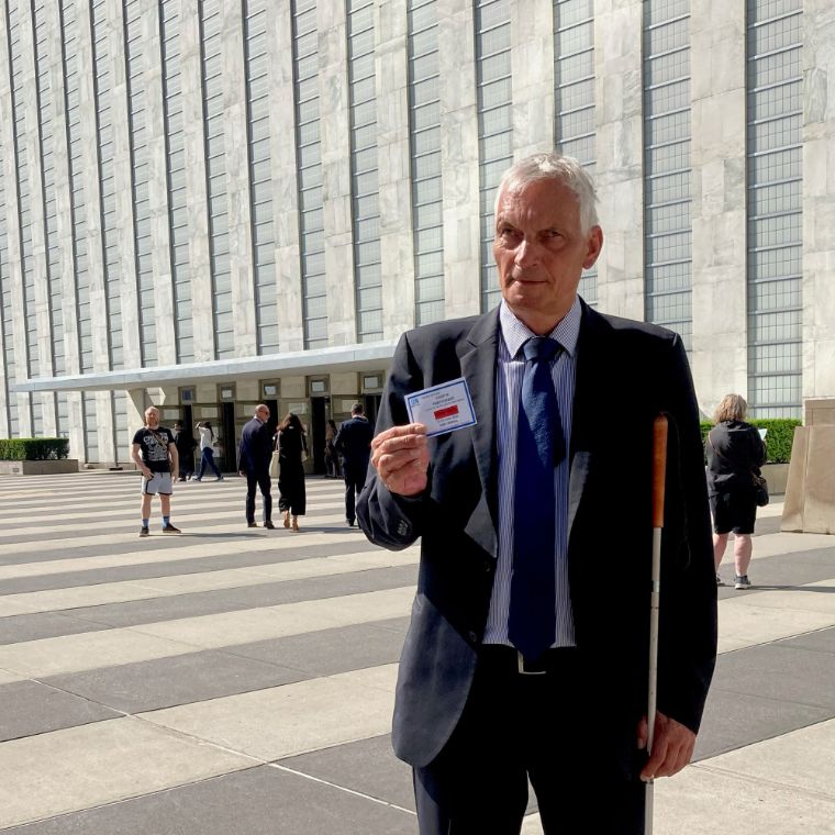 Mann mit Taststock im Anzug vor einem hohen Bürogebäude.