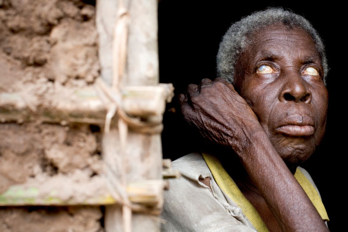 Ein alter blinder afrikanischer Mann Mann lehnt an einem Hauseingang.
