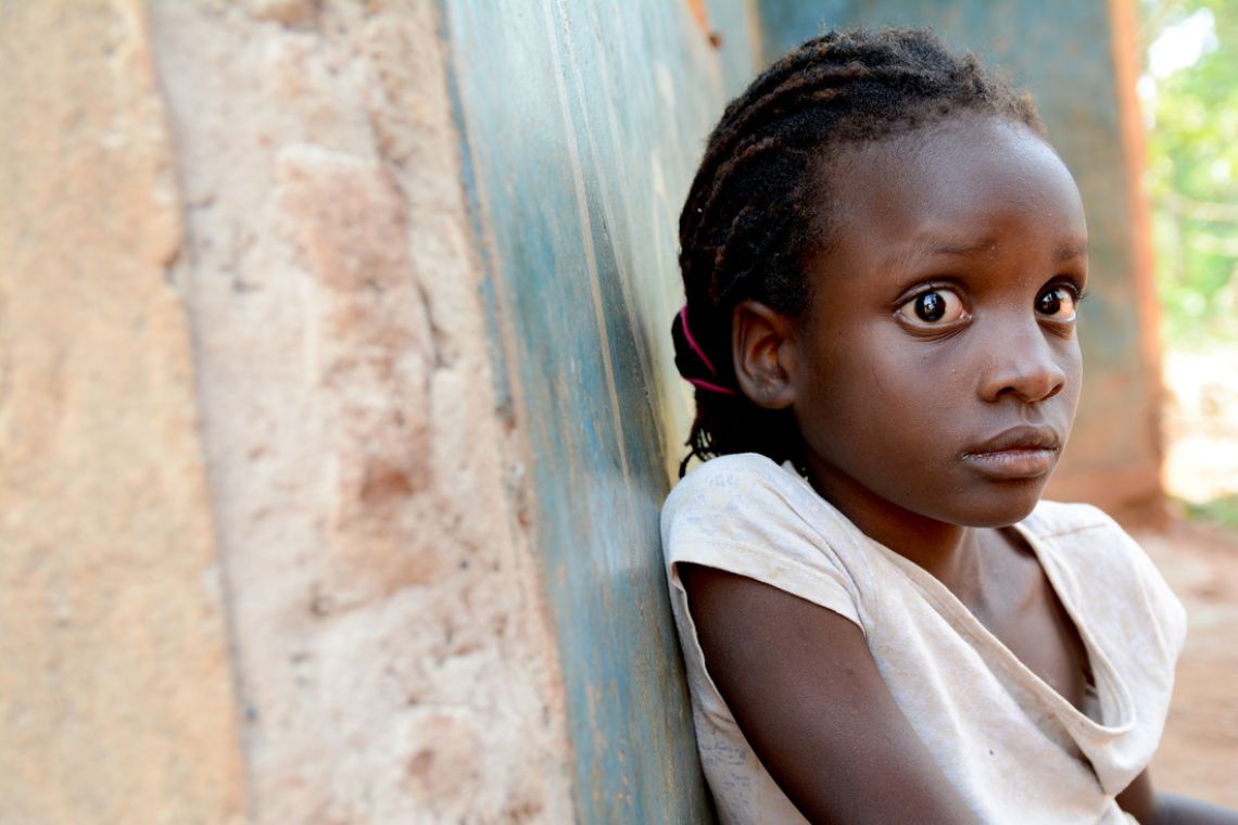 Ein blindes afrikanisches Mädchen lehnt an einer Wand.